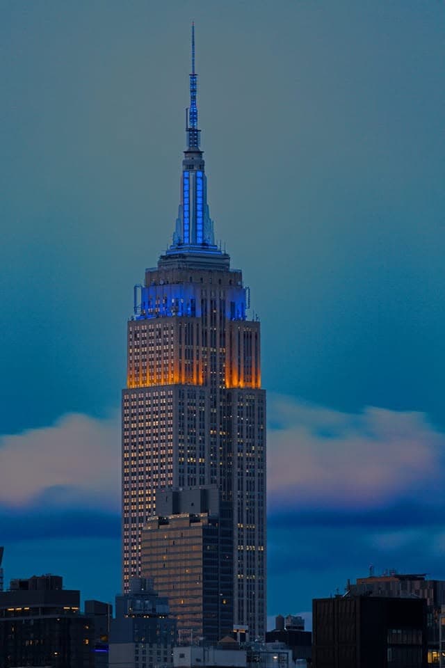Un grattacielo illuminato di blu e arancione contro il cielo dell’ora blu
